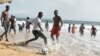 Des jeunes jouent au football devant d'autres se baignant dans la mer sur une plage de Grand-Bassam, en Côte d'Ivoire, le 28 mars 2021.