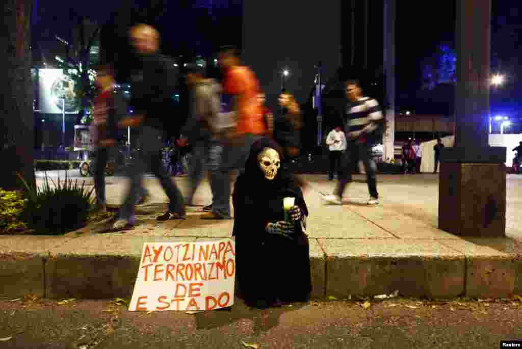 A person in a disguise sits on a sidewalk holding a candle during a protest denouncing the apparent massacre of 43 trainee teachers in Mexico City, Nov. 8, 2014. 