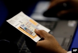 FILE - In this Feb. 26, 2014, file photo, an election official checks a voter's photo identification at an early voting polling site in Austin, Texas.