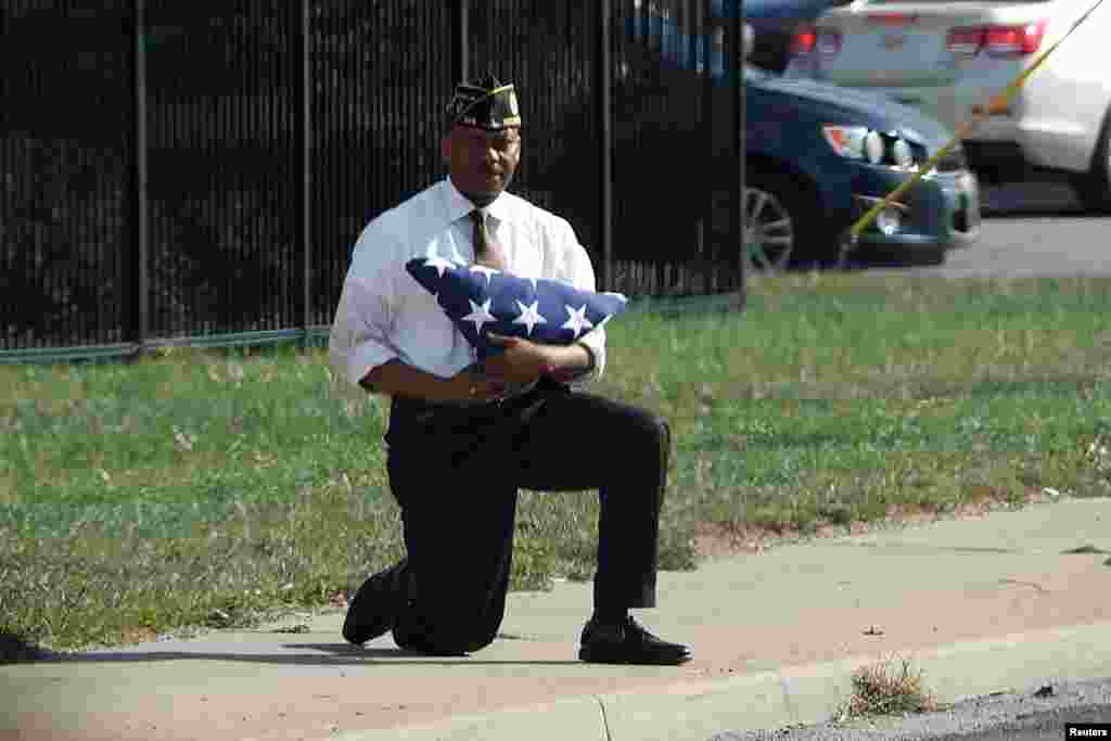 A man kneels with a folded U.S. flag as the motorcade of U.S. President Donald Trump passes him after an event at the state fairgrounds in Indianapolis, Indiana, Sept. 27, 2017.
