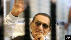 Former Egyptian President Hosni Mubarak waves to his supporters from behind bars as he attends a hearing in his retrial on appeal in Cairo, April 13, 2012. 