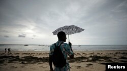 A man holds an umbrella beneath storm clouds over Wimbe beach, as the region braces for further rainfall in the aftermath of Cyclone Kenneth in Pemba, Mozambique, April 27, 2019.