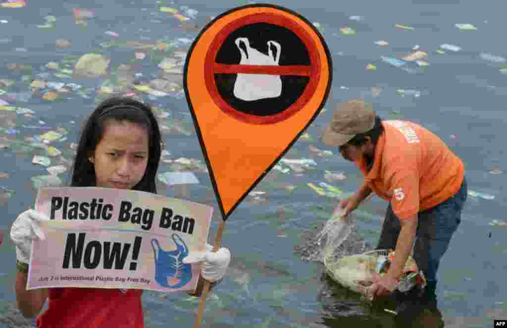 Seorang aktivis lingkungan belia di Manila, Filipina membawa plakat dengan seruan untuk melarang sampah tas plastik, sementara pekerja lingkungan membersihkan sampah plastik dari sungai.