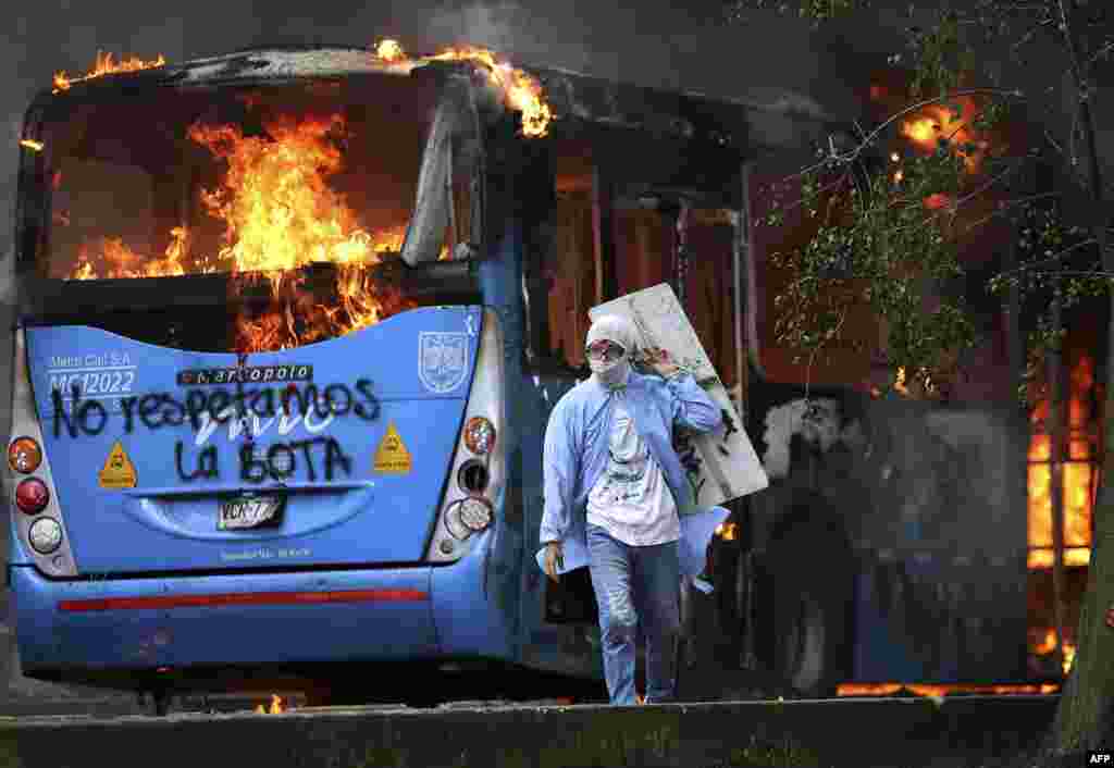 A man walks in front of a public transportation bus in flames during a protest against a tax reform bill launched by Colombian President Ivan Duque, in Cali, April 28, 2021.