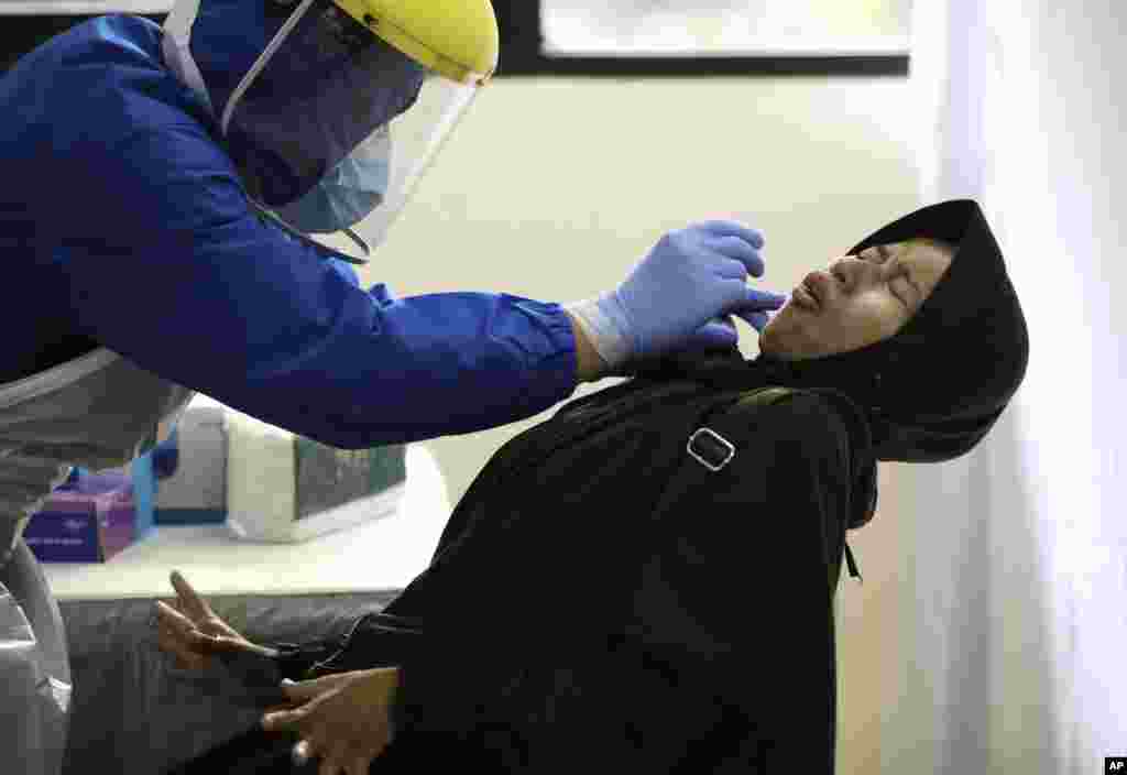 A woman reacts as she has her nasal swab sample collected by a health worker during a mass test for the new coronavirus at the local district office in Tanah Abang in Jakarta, Indonesia.