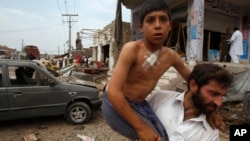 Pakistani man helps injured boy at site of car bombing on outskirts of Peshawar, Pakistan, June 30, 2013.