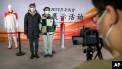 Students pose for a photo with the Olympic flame and a mannequin wearing the uniform for the Olympic torch relay during an event at the Beijing University of Posts and Communications in Beijing, Dec. 9, 2021.