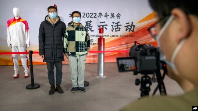 Students pose for a photo with the Olympic flame and a mannequin wearing the uniform for the Olympic torch relay during an event at the Beijing University of Posts and Communications in Beijing, Dec. 9, 2021.