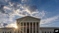 FILE - The sun flares in the camera lens as it rises behind the U.S. Supreme Court building in Washington, June 25, 2017.