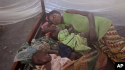 FILE - Two children and their mother rest under a mosquito net.