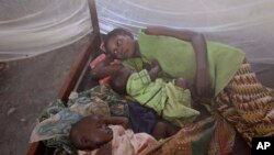 FILE - Two children and their mother rest under a mosquito net in the small village of Walikale, Congo.