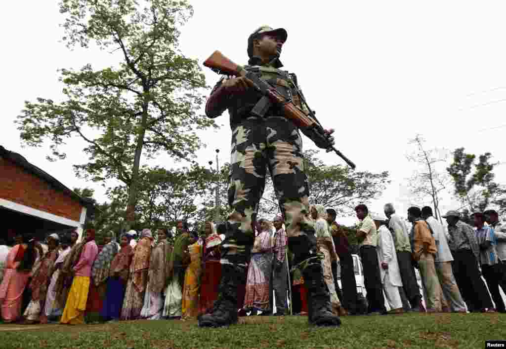 Um militar está de guarda, enquanto as pessoas formam fila para votar na vila de Nakhrai em Tinsukia, um distrito no Estado de Assam, Abril 7, 2014.