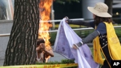 Một phụ nữ tìm cách dập lửa cho người đàn ông tự thiêu trước sứ quán Nhật Bản ở Seoul, ngày 12/8/2015.