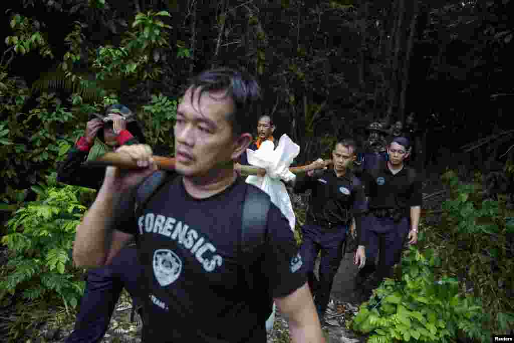 Members of a police forensic team carry a body bag with human remains dug from a grave near the abandoned human trafficking camp in the jungle close to the Thailand border at Bukit Wang, Burma, in northern Malaysia, May 27, 2015.