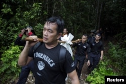 Members of a police forensic team carry a body bag with human remains dug from the grave near the abandoned human trafficking camp in the jungle close the Thailand border at Bukit Wang Burma in northern Malaysia , May 27, 2015.