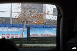 In this Dec. 5, 2018, photo, slogans which reads "Technical skill in hand, No worries finding a job," are seen on the barbed wire fences around the "Hotan City apparel employment training base" where Hetian Taida has a factory in Hotan.