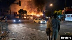 2020年5月28日，美国明尼阿波利斯骚乱事件中抗议者注视一家汽车零件商店在燃烧。