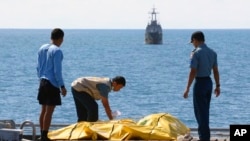 Para anggota tim pencari korban AirAsia memeriksa kantung jenazah di dek kapal Angkatan Laut KRI Banda Aceh, di laut Jawa, Indonesia (23/1).