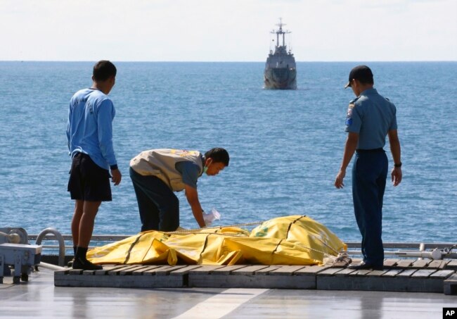 Awak kapal memeriksa tas berisi jenazah yang diyakini korban Penerbangan AirAsia 8501 di geladak kapal TNI AL KRI Banda Aceh, di Laut Jawa, Jumat 23 Januari 2015. (Foto: AP)