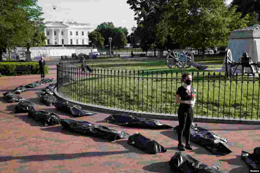 Margot Bloch stands in a line of mock body bags while holding flowers during a funeral procession demonstration for the COVID-19 victims outside of the White House in Washington, May 20, 2020.