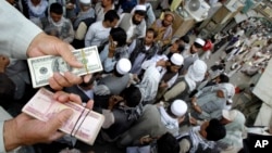 An Afghan trader holds U.S. dollar and Afghani bundles at the Saray- e Shahzadeh, the main exchange market in Kabul, Afghanistan, Sept. 18, 2011.