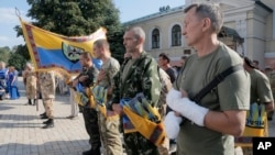 FILE - Volunteers of battalion 'Donbas' hold battalion flags during a blessing ceremony in St. Michael Cathedral in Kyiv, Ukraine.