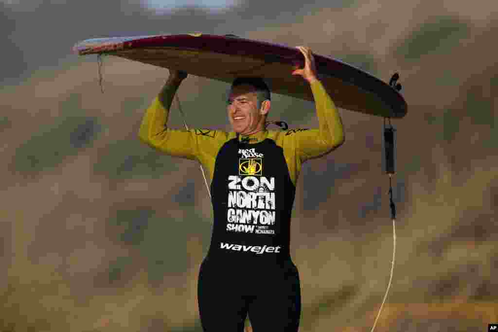 Peselancar AS Garrett McNamara mengangkat papan selancarnya setelah menaiki ombak di pantai Praia do Norte di Nazare, Portugis (29/1). (AP/Francisco Seco)