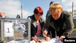 Местный житель подписывает документы на получение бюллетеня от члена (слева) местной избирательной комиссии во время "референдума" о статусе Луганской области, 11 мая 2014 года (иллюстративное фото)