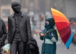 FILE - A youth wearing a face mask looks up at statue of John Lennon, part of a larger statue of The Beatles in Liverpool, England, Monday Oct. 12, 2020, as Prime Minister Boris Johnson prepares to lay out a new three-tier alert system for England.