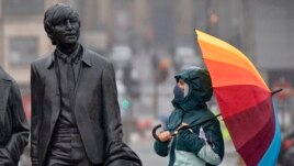 FILE - A youth wearing a face mask looks up at statue of John Lennon, part of a larger statue of The Beatles in Liverpool, England, Monday Oct. 12, 2020, as Prime Minister Boris Johnson prepares to lay out a new three-tier alert system for England.