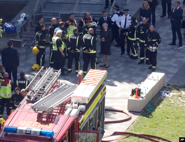 Britain's Prime Minister Theresa May, center, speaks with firefighters after arriving at Grenfield Tower in London, June 15, 2017, following a deadly fire in the apartment block.