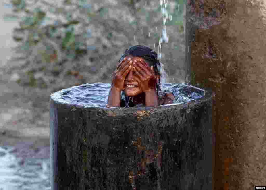 A girl bathes to cool herself off with water that is leaking from a broken pipe valve on a hot summer day on the outskirts of Ahmedabad, India, May 18, 2015.
