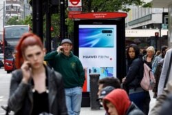 FILE - Pedestrians use their mobile phones near a Huawei advertisement at a bus stop in central London, April 29, 2019.