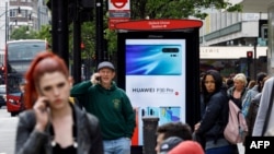 FILE - Pedestrians use their mobile phones near a Huawei advertisement at a bus stop in central London, April 29, 2019.