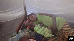 FILE - Two children and their mother rest under a mosquito net.
