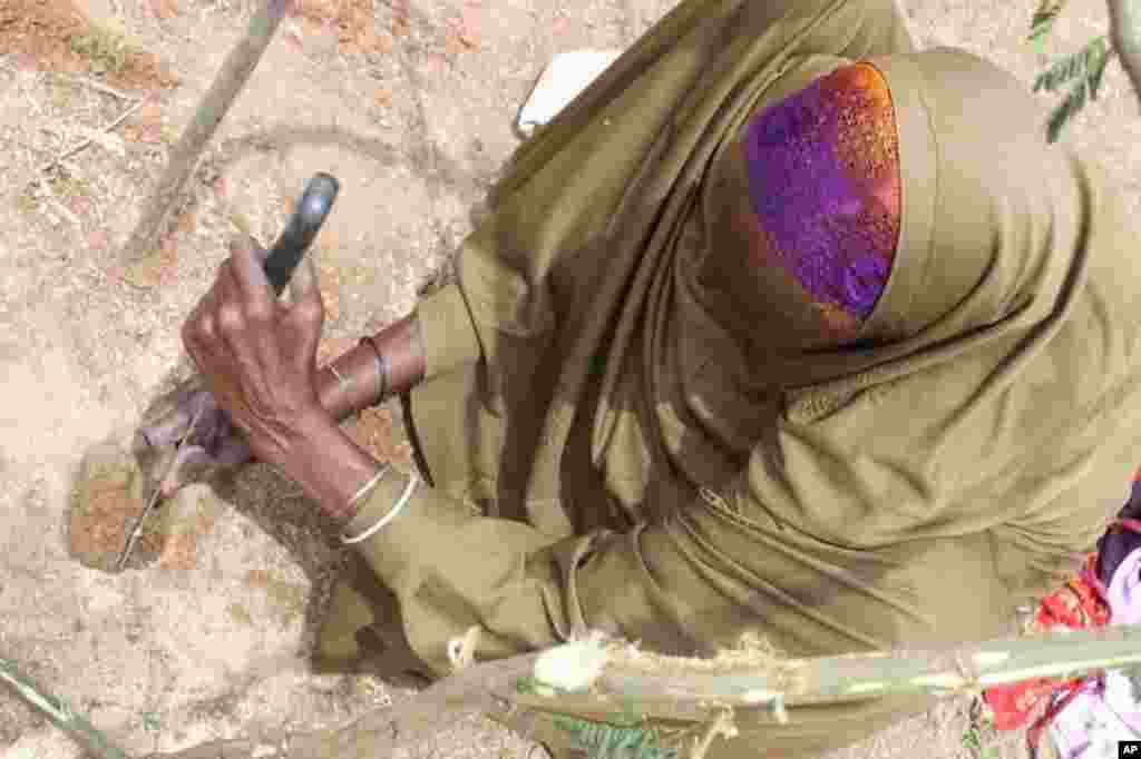 A. woman digs hole to plant a branch that will serve as the tent structure of her new IDP home. (VOA - P. Heinlein)