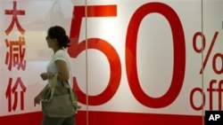 Seorang pejalan kaki melintasi papan reklame di sebuah pusat perbelanjaan di Beijing, Tiongkok (9/8). Laju inflasi Tiongkok turun tajam bulan Juli, memberikan keleluasaan bagi pemerintah untuk melonggarkan kebijakan fiskan dalam menstimulasi pertumbuhan e