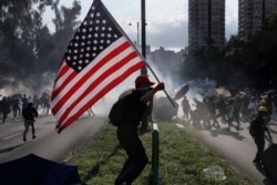 FILE - A protester runs with a United States flag as tear gas is released on protesters in Hong Kong, Aug. 5, 2019.