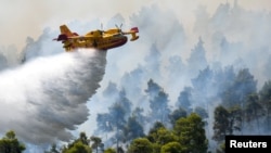 A firefighting airplane makes a water drop as a wildfire burns near the village of Ellinika, on the island of Evia, Greece, Aug. 8, 2021.