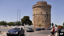 Striking taxi owners drive past the White Tower of Thessaloniki, the northern Greek city's main landmark, during a protest against certain austerity measures, as tourists look on, July 21, 2011