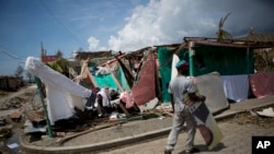 A man carries a presidential election poster past a destroyed kindergarten in Les Anglais, Haiti, Oct. 10, 2016. Presidential elections scheduled for the previous day were postponed after the passage of Hurricane Matthew.