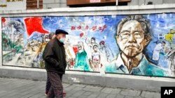 FILE - Residents wearing masks pass a mural titled "Memories" on the eve of the anniversary of the 76-day lockdown in the central Chinese city where the coronavirus was first detected, in Wuhan, Hubei province, Jan. 22, 2021. 