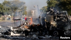 Locals walk past a shell of a burnt out truck used to barricade roads by protesters in Atteridgeville, a township west of Pretoria, South Africa, June 21, 2016.