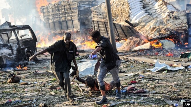 Two men carry the body of a victim following the explosion of a truck bomb in the center of Mogadishu, on Oct. 14, 2017.