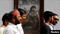 People walk past a poster of an Indian movie "Baahubali: The Beginning" outside a movie theater in New Delhi, India, April 12, 2017. 
