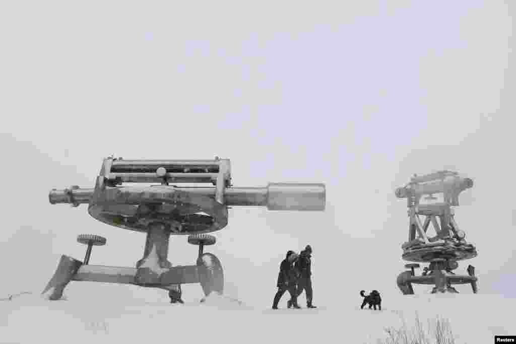 People walk with a dog next to Terris Novalis sculptures during snowfall in Consett, Britain.