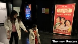 People walk past a poster for the Chinese movie 'Hi, Mom,' which opened on the first day of the Lunar New Year, at a cinema in Beijing, China, Feb. 19, 2021. 
