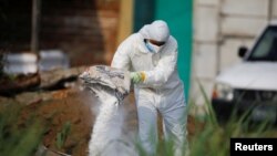 Un experto forense arroja cal sobre el equipo de protección desechado utilizado donde las autoridades están excavando un cementerio clandestino descubierto en la casa de un ex policía y que contiene hasta 40 cadáveres, El Salvador, 20 de mayo. 2021.