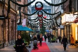 People walk past shops under Christmas decorations during the novel coronavirus pandemic in Stockholm, Dec. 3, 2020.