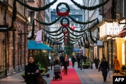 People walk past shops under Christmas decorations during the novel coronavirus pandemic in Stockholm, Dec. 3, 2020.